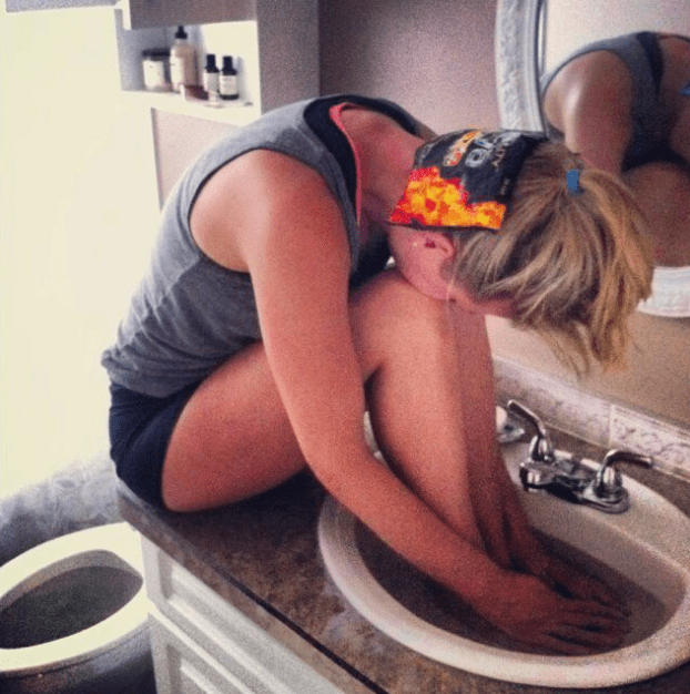 this is a picture of a lady with her hands and feet in a sink of warm water and a bag of frozen peas on her neck, which is said to be a home remedy for curing migraines.