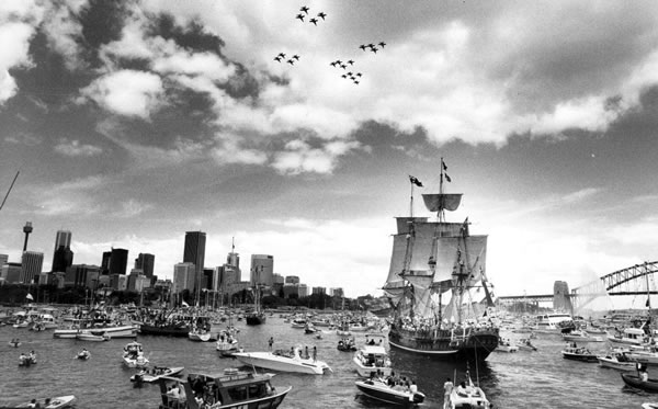 a black and white photo of a tall ship coming into Sydney Harbor surrounded by several other boats